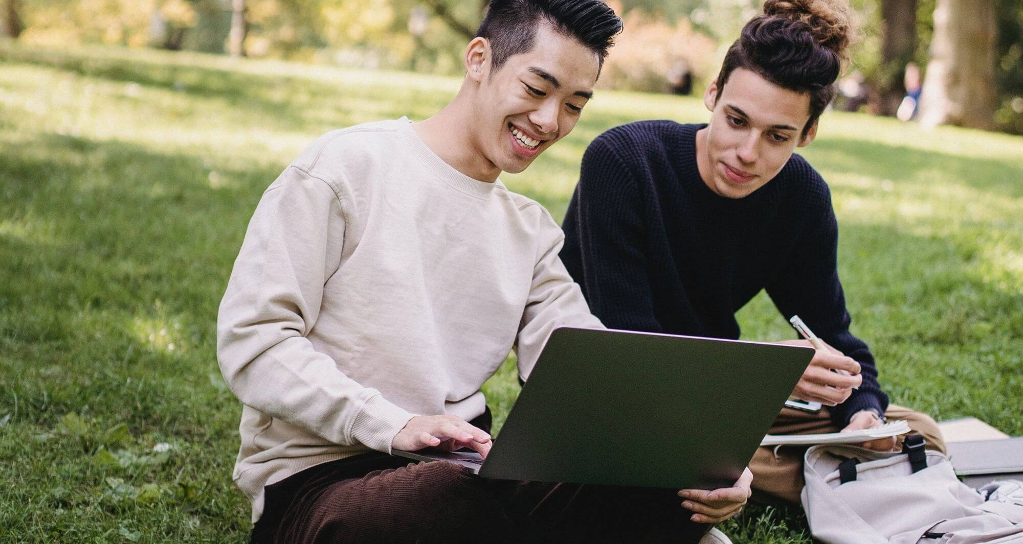 Two residents sitting on grass while working on laptop